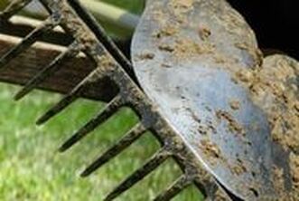 A very close up picture of the bottom of a rake and a shovel side by side. Both of them are covered in dirt. 
